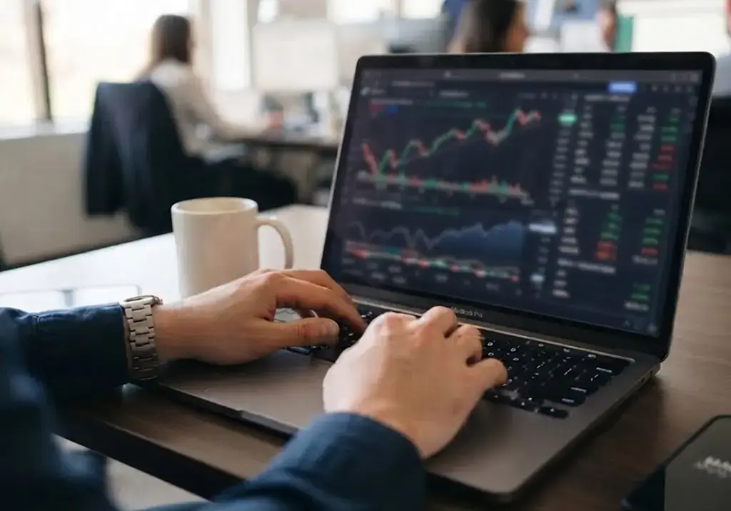 Hands typing on a laptop displaying financial charts and data