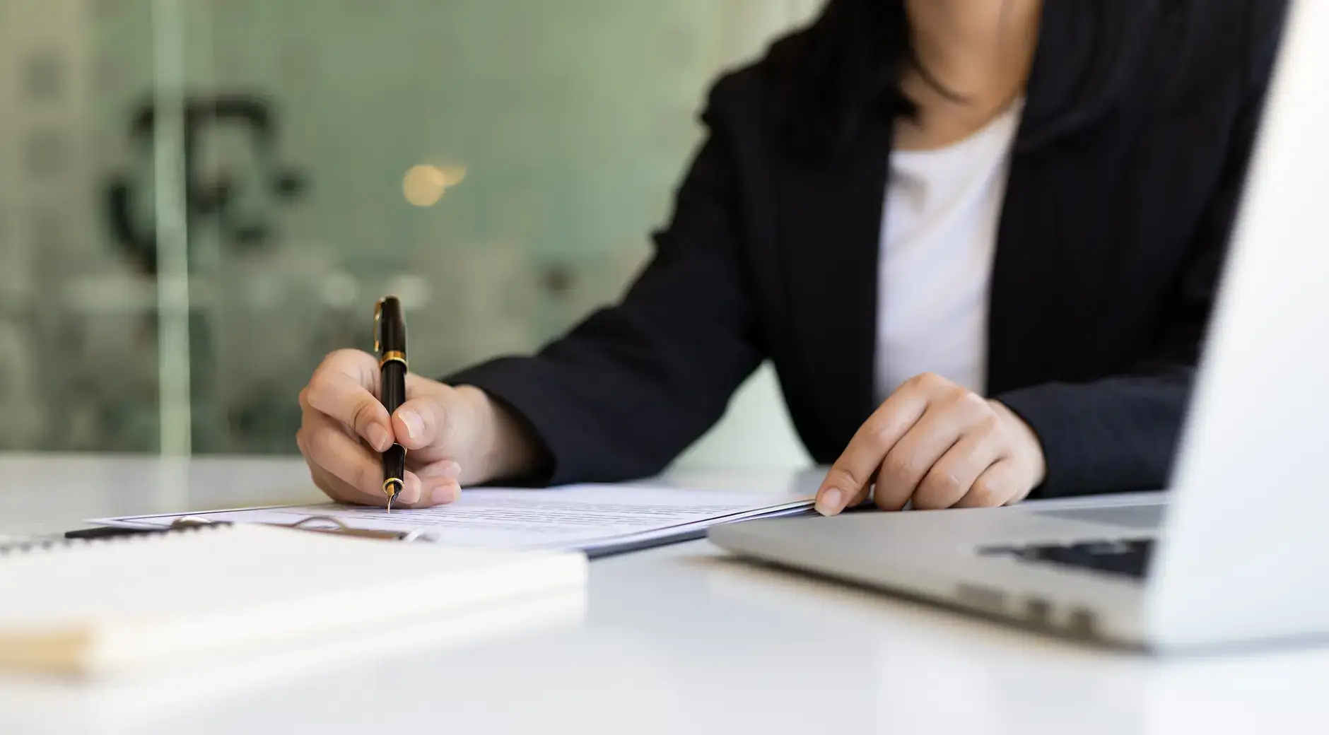 Businesswoman signing a document at her desk next to a laptop