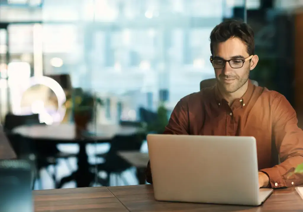 Man working on a laptop in a modern glass-walled office.