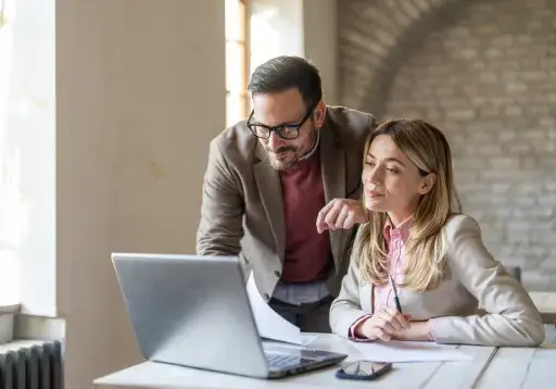 Man and woman reviewing data together on a laptop at a desk.